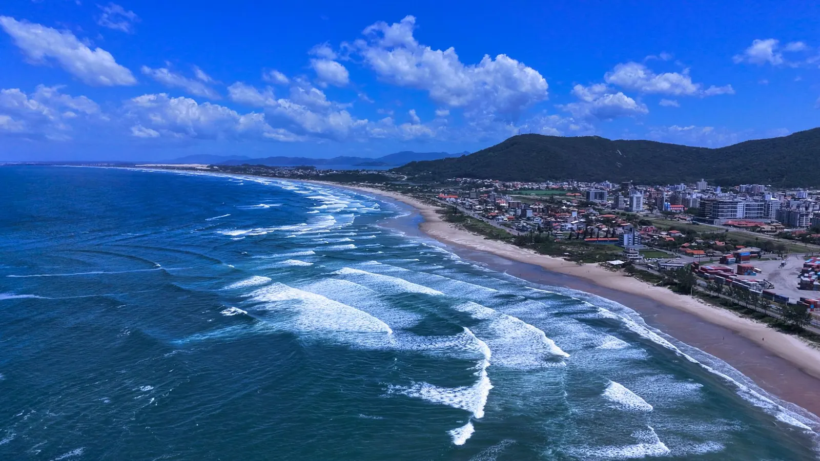 Vídeo aéreo do litoral de Imbituba, com praia, ondas e morro.