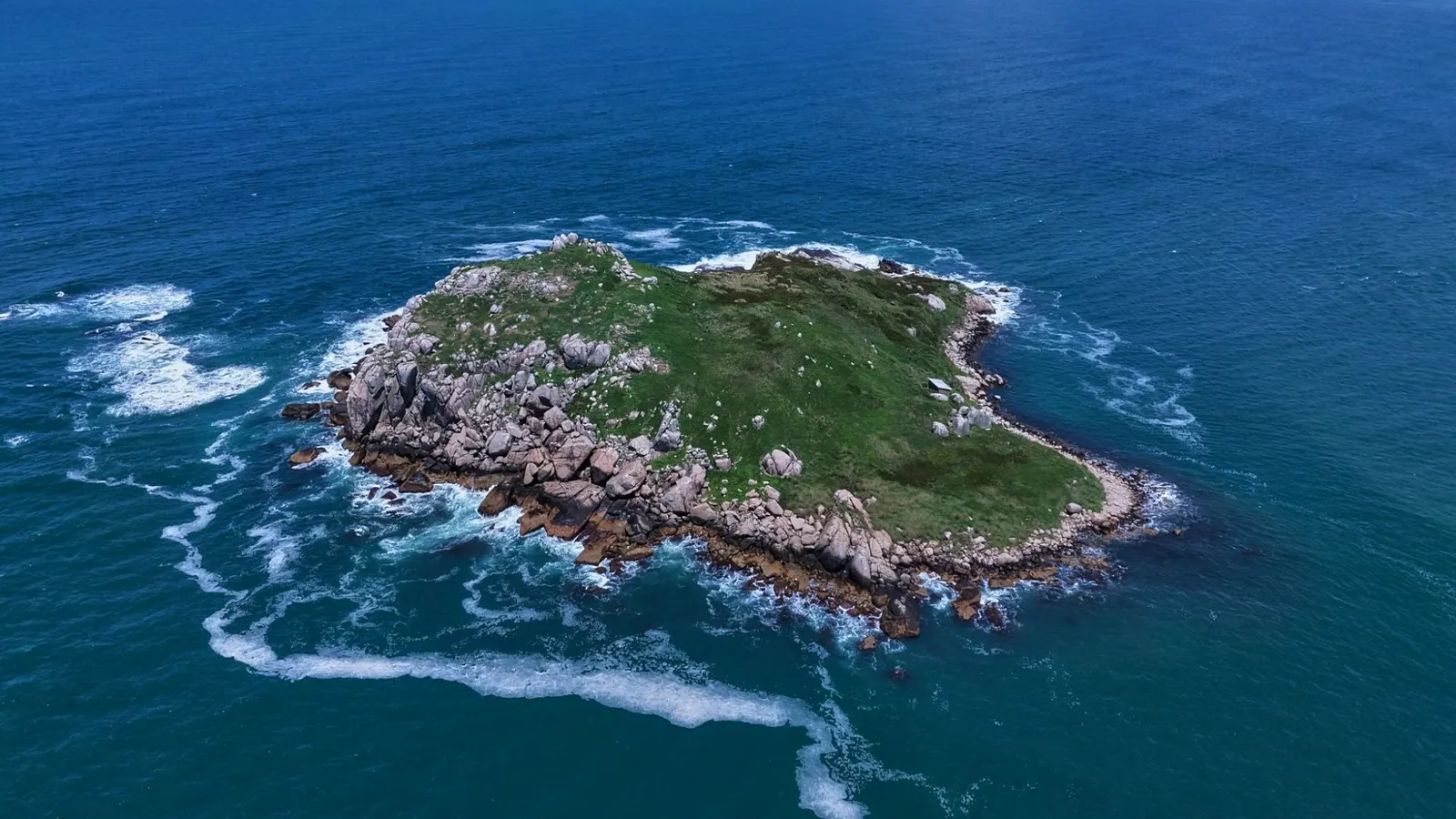 Vista aérea de uma ilhota rochosa cercada pelo mar.